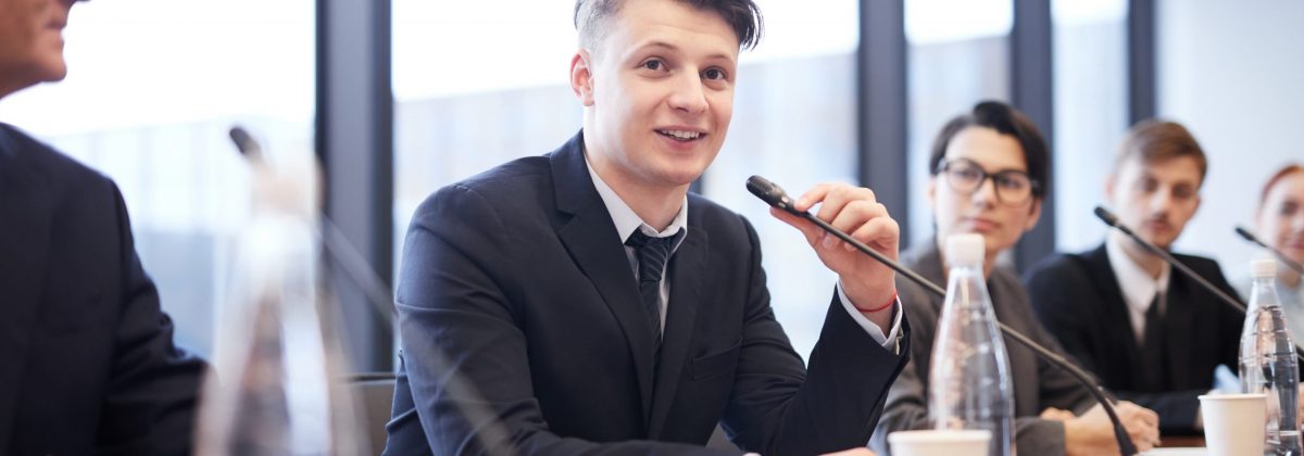 Portrait of smiling businessman speaking to microphone during press conference or training seminar, copy space